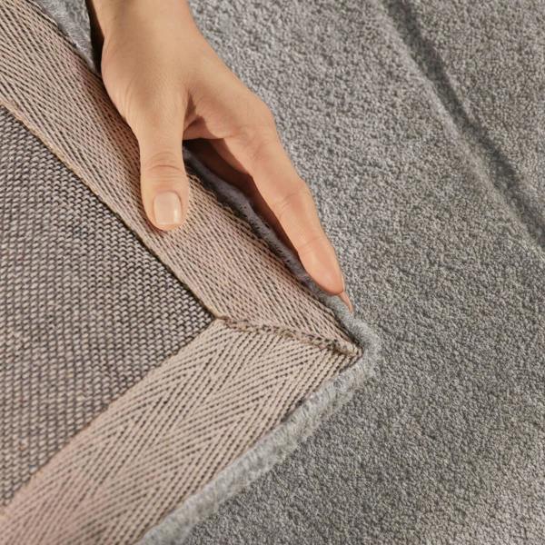 Close-up of a hand touching the edge of a textured gray rug.