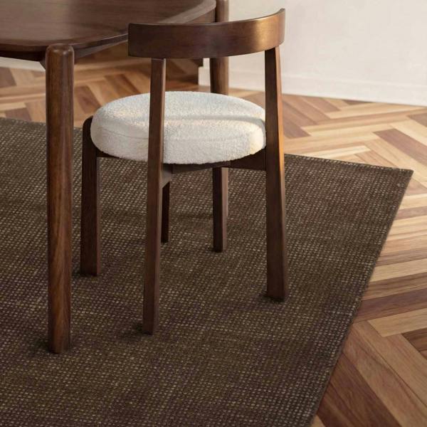 Wooden chair with a white cushion on a brown rug in a room with wooden flooring.