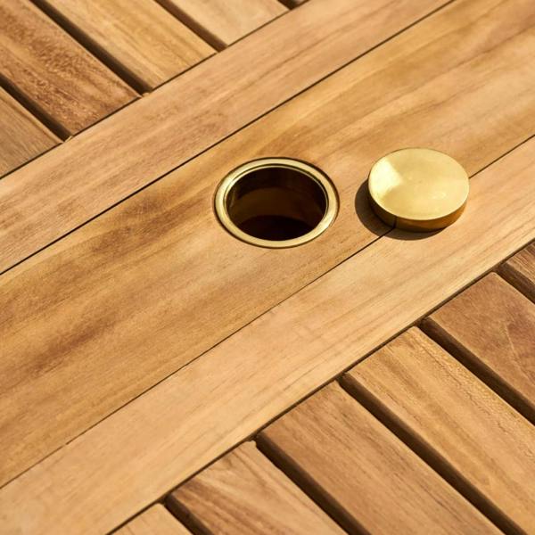 Close-up of the brass-fitted parasol hole on a teak tabletop with the matching brass cap sitting nearby.