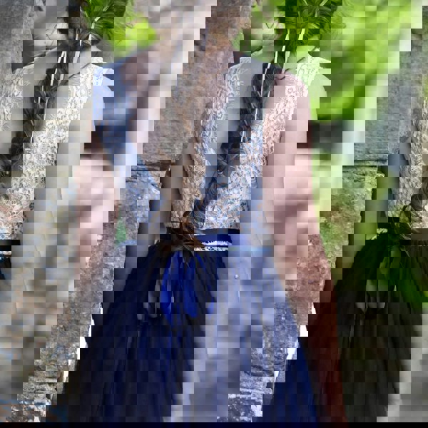 Girl wearing a white lace top and navy blue skirt with a blurred natural background