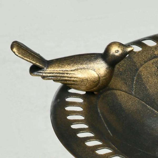 Bronze-tone decorative bird ornament perched on the edge of a bird bath bowl