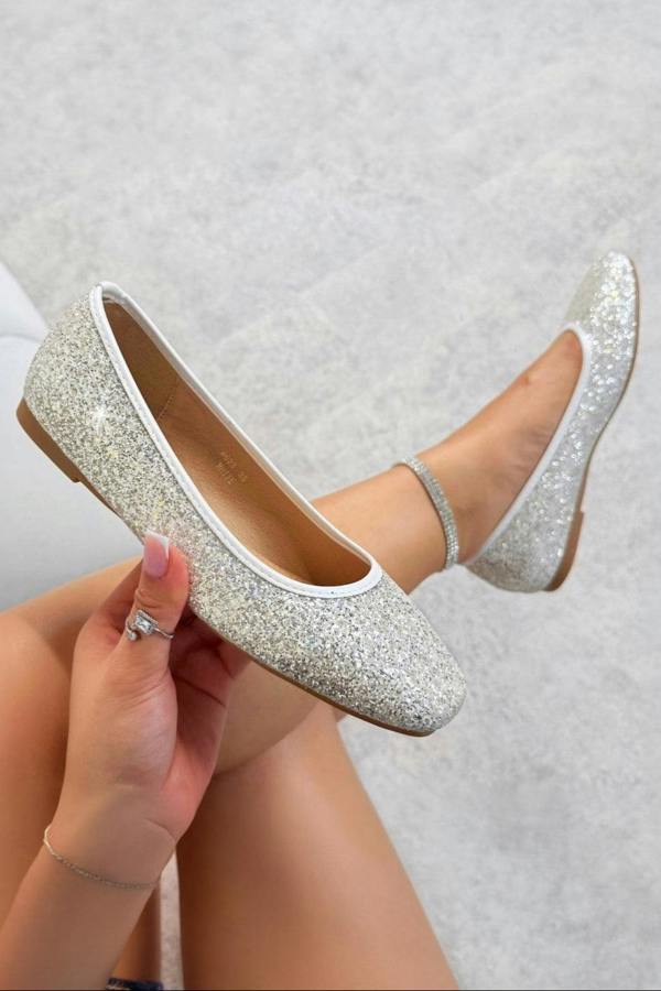 White glittery flats worn by a person on a light gray background