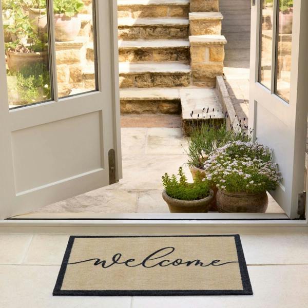 Welcome mat in front of a door with plants and steps leading outside