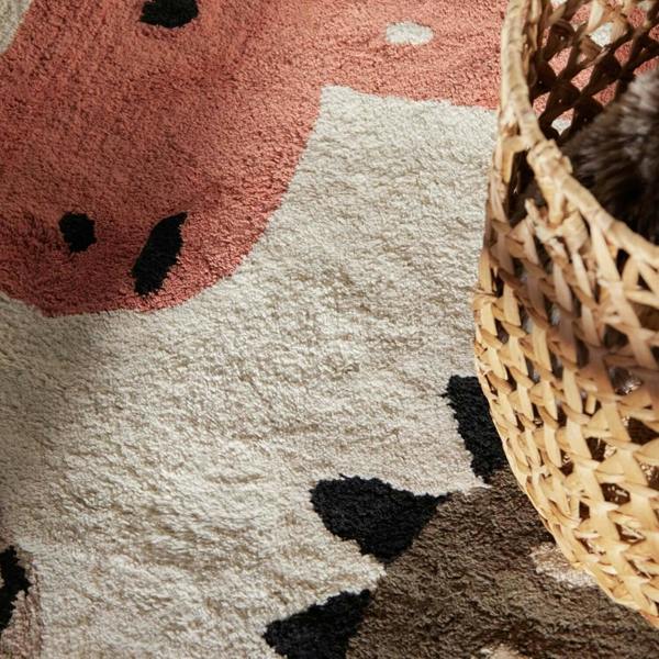 Close-up of a cow-patterned rug with a wicker basket on a pink and white background