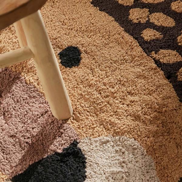 Close-up of a textured multicolored rug with a wooden stool leg.