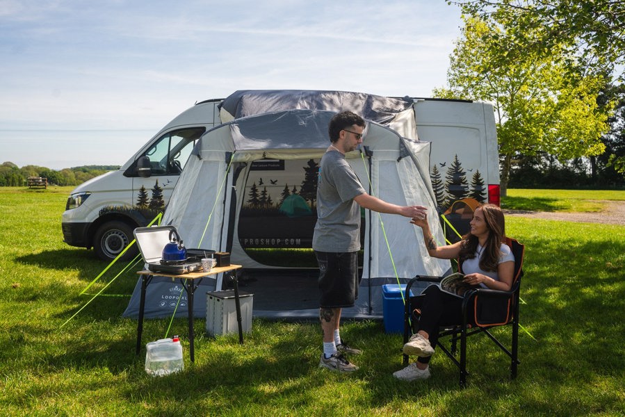 A couple shares a drink outside of the Loopo Breeze® XL v2 Motorhome Awning, they are using OLPRO camping furniture