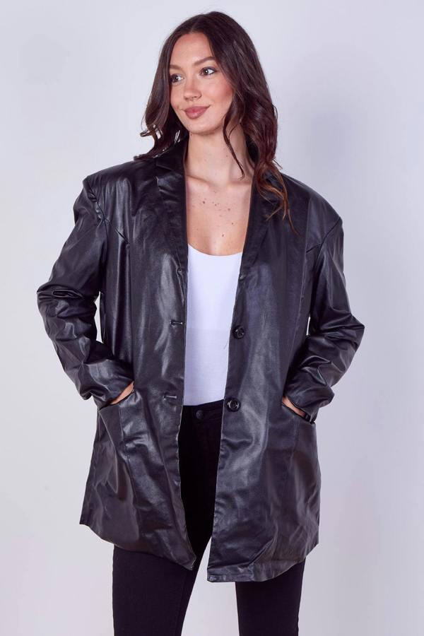 A woman modeling an oversized black faux-leather blazer with a glossy finish, worn open over a white top and black pants, against a light gray studio background.