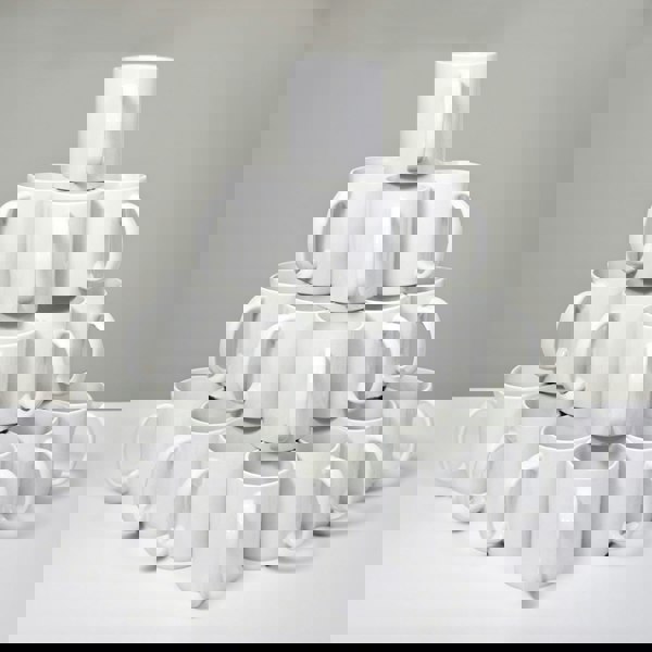 Stack of 36 plain white ceramic mugs arranged in pyramid shape on gray background.