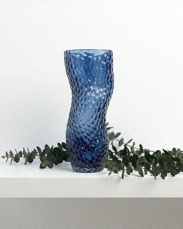 Blue textured vase on a light gray surface with a book titled 'Interior Living'.