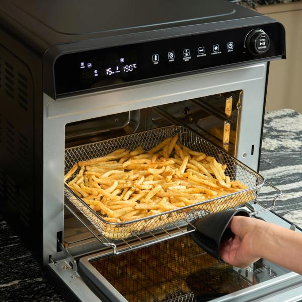 A hand wearing an oven mitt pulls out a basket of French fries from the Fridja f77 Super Oven Pro - 30L Digital Air Fryer Oven in a modern kitchen.