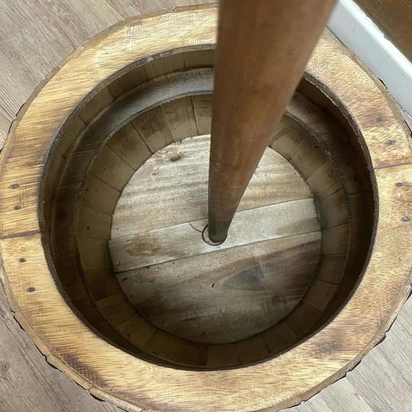 Natural wood umbrella pole base inside circular barrel tabletop opening