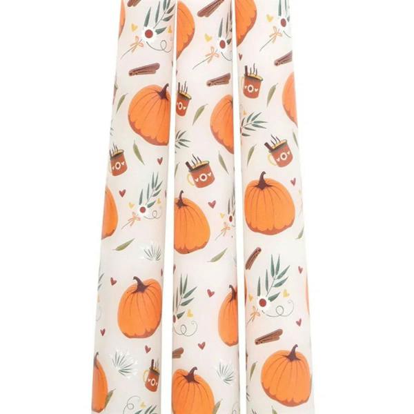 Close-up of white taper candles with orange pumpkin, leaf, and twig pattern
