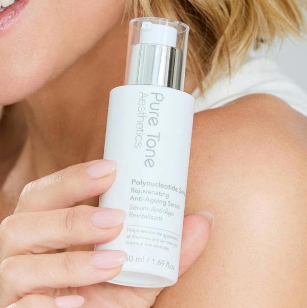A close-up of Kimberley Walsh holding a white bottle of Pure Tone Aesthetics Polynucleotide Serum against her shoulder.