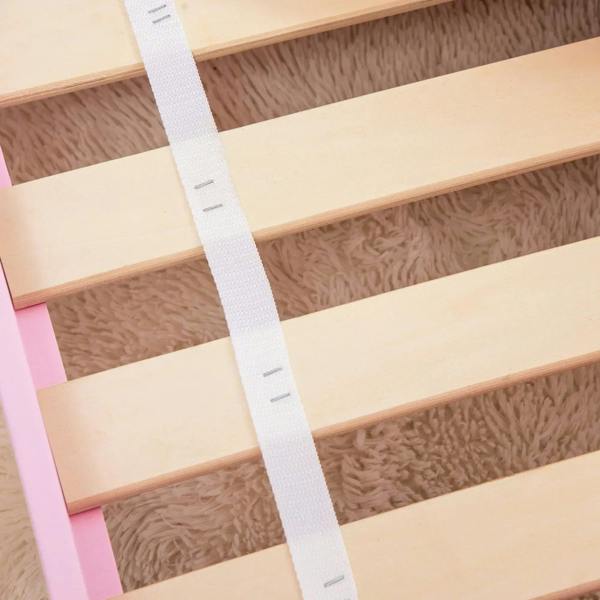 Wooden bed slats inside a pink toddler bed frame with side guard rail posts