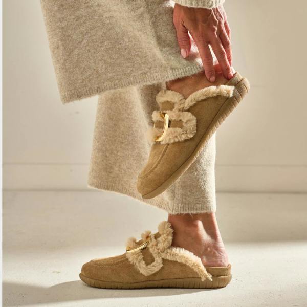 Person wearing beige slippers with fur trim on a neutral background