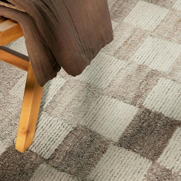 Close-up of a checkered patterned carpet with a wooden chair leg and brown fabric.