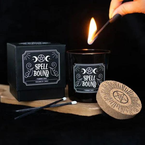 Lit black candle jar with cork lid and white occult label, with matchstick nearby