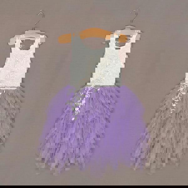 White top and purple tutu skirt dress on a hanger against a brown background