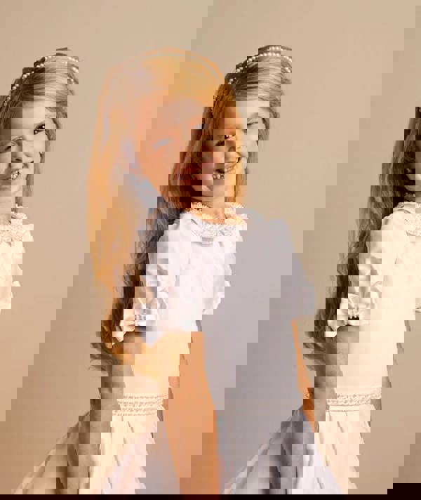 Young girl wearing a white dress with a bow on a beige background