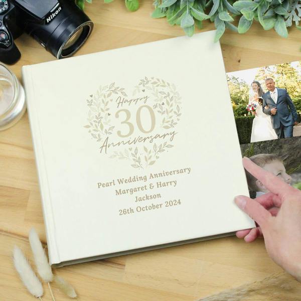 A cream-coloured 30th Pearl Wedding Anniversary photo album resting on a wooden surface, featuring a floral heart design with the text '30th Anniversary', 'Pearl Wedding Anniversary', and the names 'Margaret & Harry Jackson'.