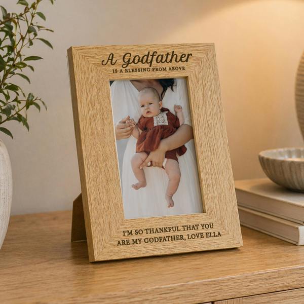 An engraved oak veneer photo frame displaying a baby in a white christening outfit, styled on a wooden console table with neutral home decor.