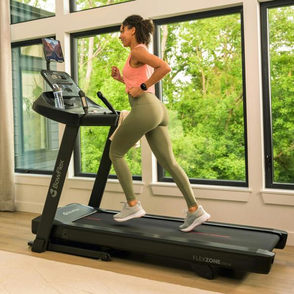 Woman running on a BowFlex T6 treadmill in a bright home gym setting.