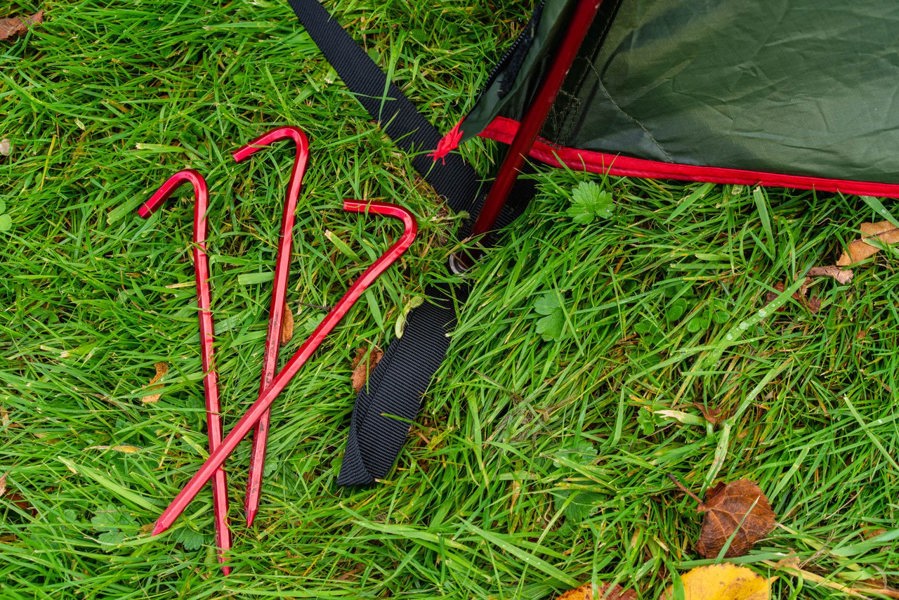 The Beckford Lightweight 2 Person Tent 's red anodised pegs on grass, next to a ring and pin system.