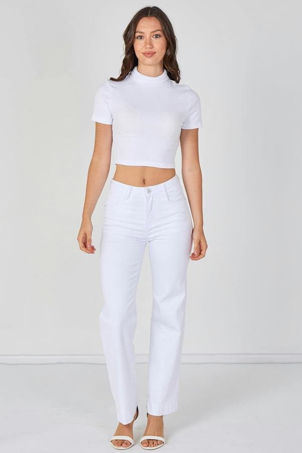 Woman wearing a white crop top and white pants on a plain background