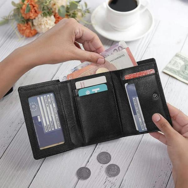 Person opening a black wallet with cards and money on a wooden table.