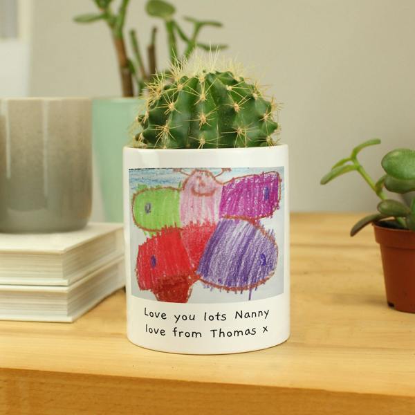 A custom white ceramic pot featuring a bright child's crayon drawing of a butterfly and a personalized message printed below, styled with a small cactus inside.