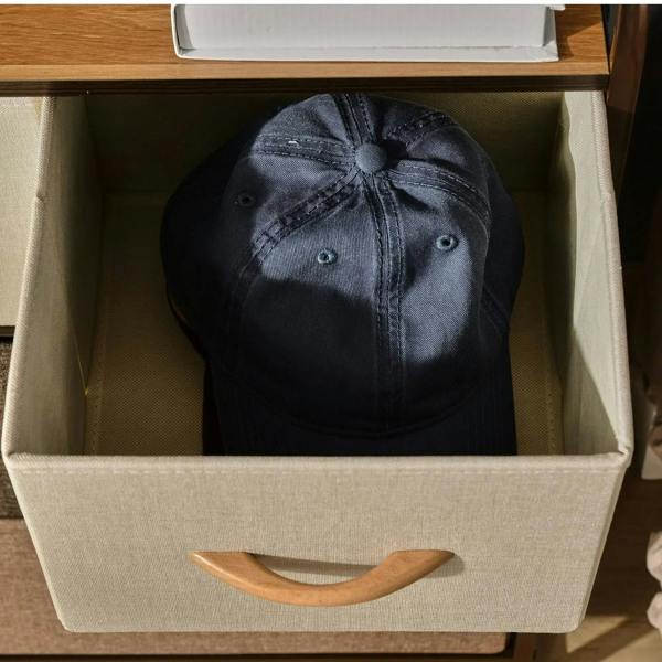 Open fabric drawer holding a dark baseball cap, curved wooden handle, inside view