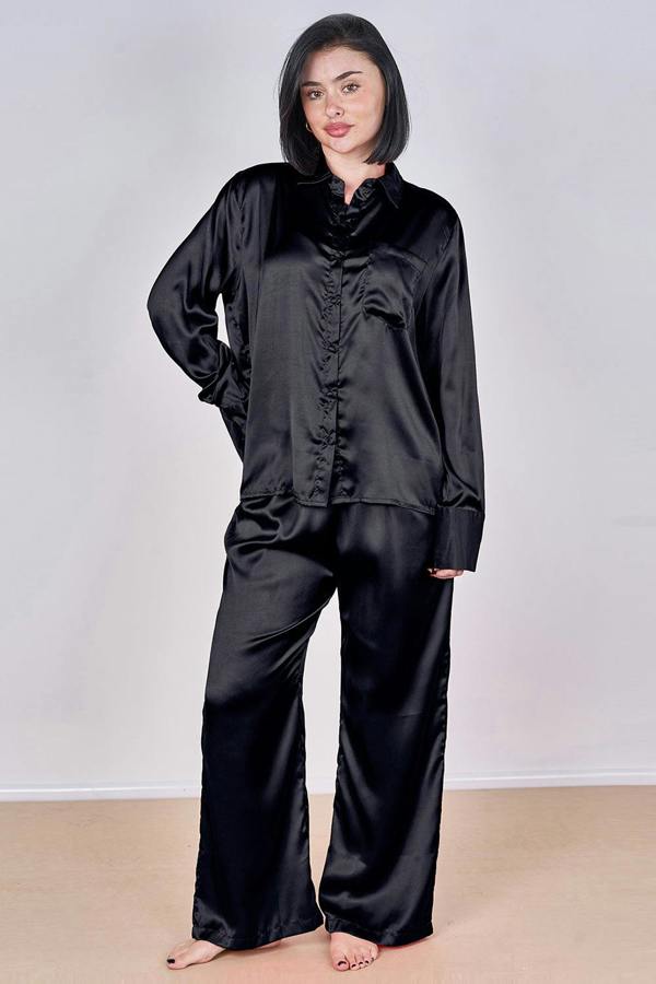 Woman wearing a black satin pajama set against a plain background