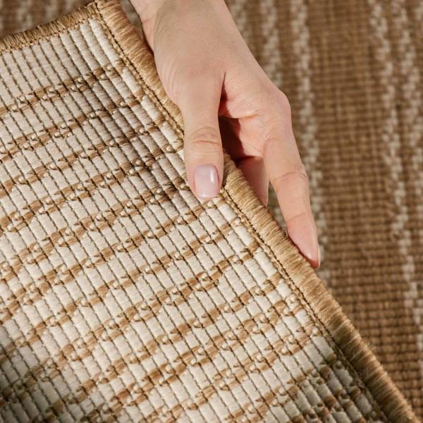 Close-up of a hand touching a textured brown and beige rug