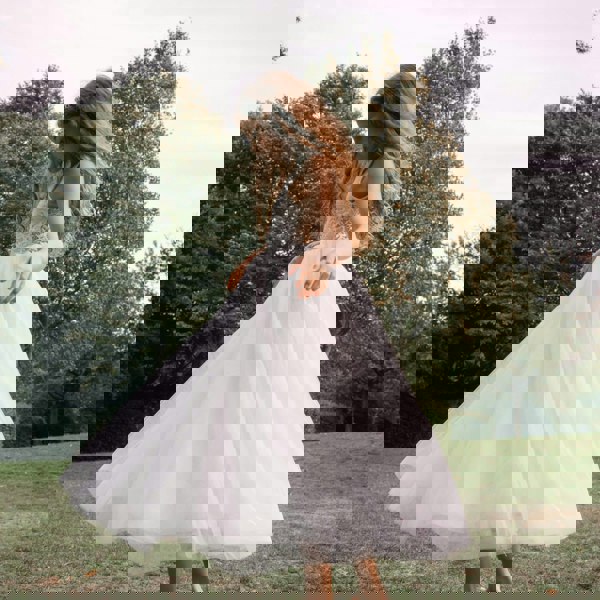 girl in a white dress standing in a park with trees in the background