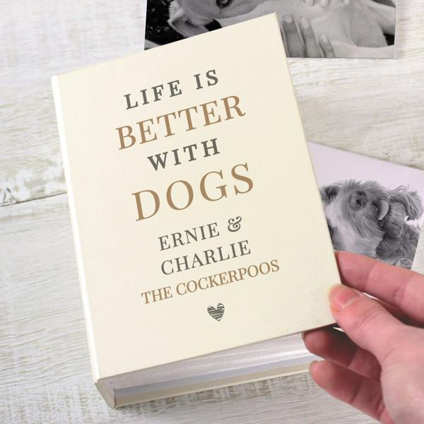 A square, cream-coloured personalised photo album with the text "LIFE IS BETTER WITH MINNIE ALWAYS BY OUR SIDES SINCE 2023" printed in brown font. The album is resting on brown paper with a white mug of coffee on a saucer and a white knit blanket visible in the background.