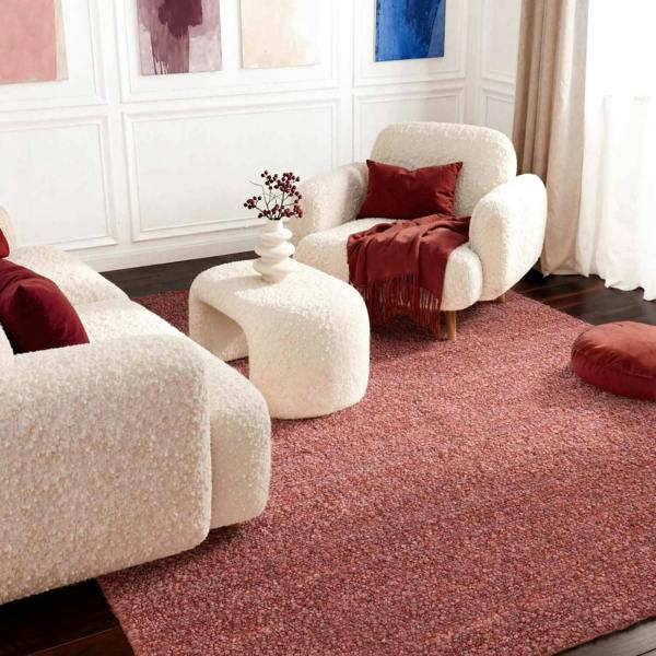 Living room with white armchairs, a red rug, and decorative pillows.