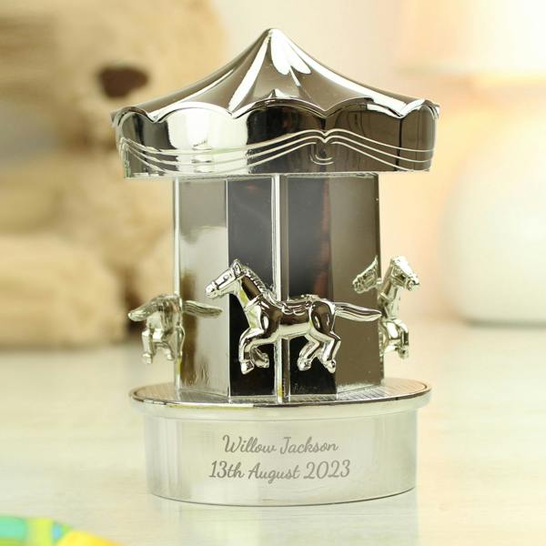 A high-shine silver-plated carousel money box engraved with 'Willow Jackson 13th August 2023' sitting on a bright nursery tabletop.