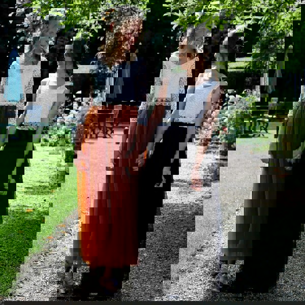 Two girls in formal dresses standing on a gravel path with greenery in the background