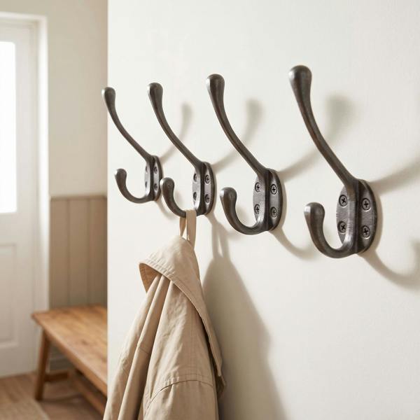 Close-up of Victorian-style iron wall hook on off-white wall with jacket hanging, highlighting craftsmanship and antique matte finish.