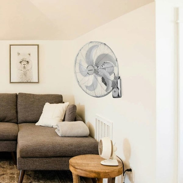 The Senelux 16 inch chrome wall mounted fan attached to a wall in a home above a corner-sofa