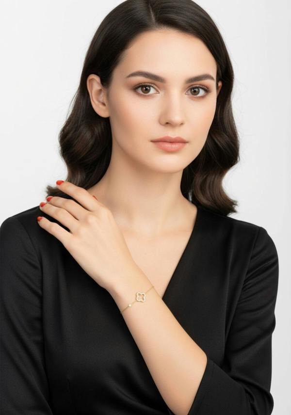 Woman wearing a gold clover  bracelet on a plain background