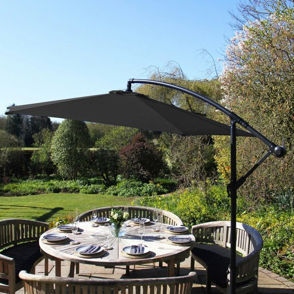 Anthracite 4 piece sofa set with a sleek black parasol, featuring a sturdy base, set against a lush garden backdrop