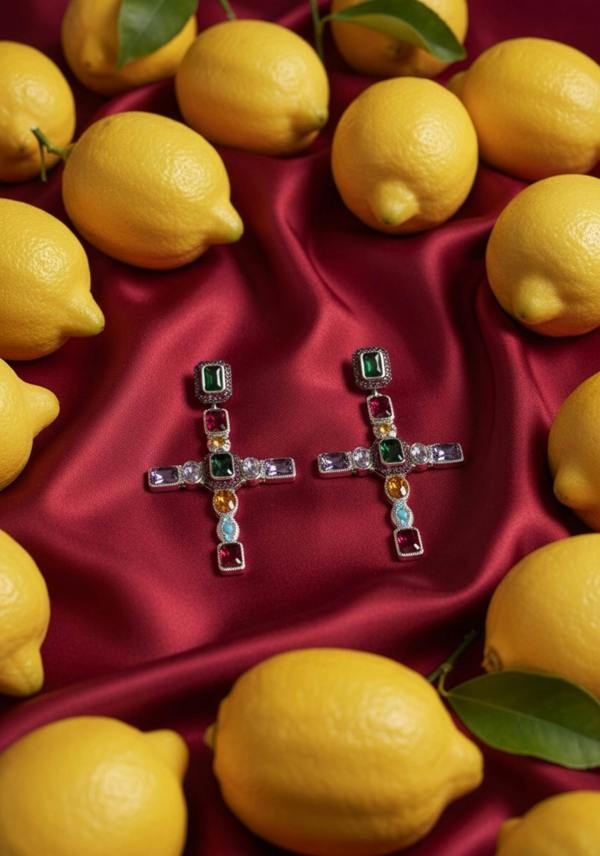 Cross shaped earrings with multicoloured gemstones on red fabric surrounded by lemons