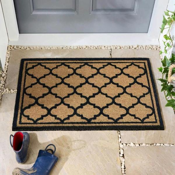 Decorative doormat with geometric pattern on a stone floor in front of a door.
