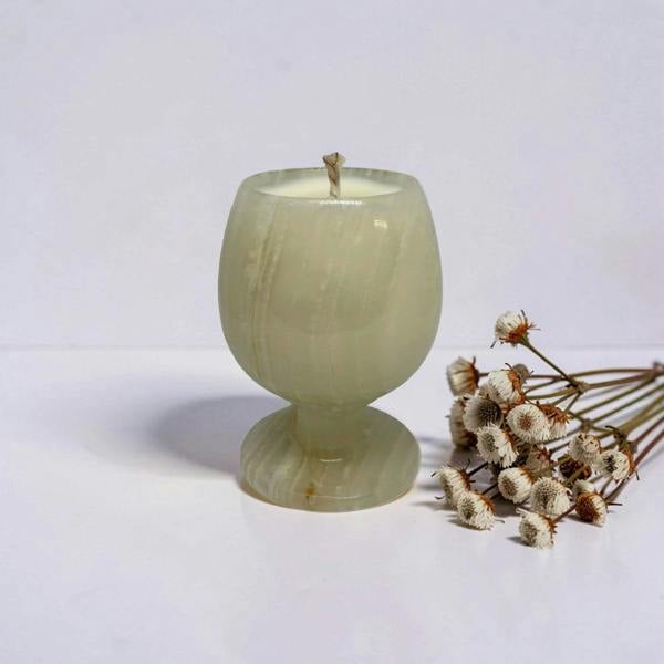 Green candle in a textured holder with dried flowers on a light gray background