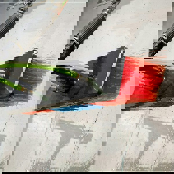 Red and blue bristle brush with green hoses, spraying water, attached to a 20ft cleaning pole for outdoor cleaning tasks