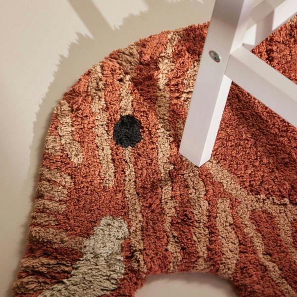 Textured red and beige rug with a white chair leg on a light-colored floor.