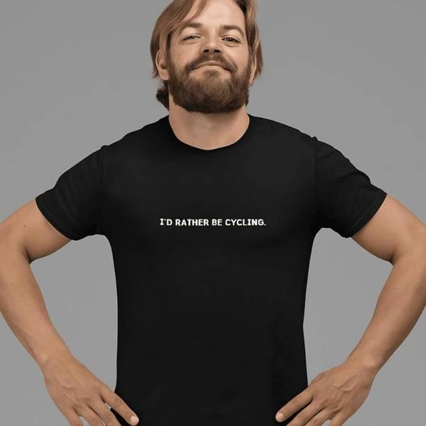 A man in a black unisex t-shirt with white text across the chest that reads "I'D RATHER BE CYCLING." set against a grey background.