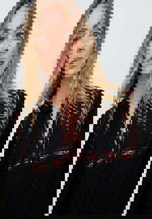 Woman wearing a black dress with colorful embroidery on a white background