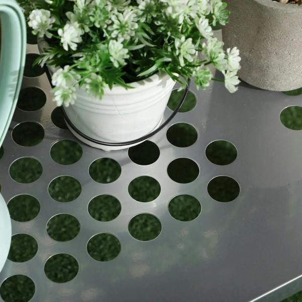 Perforated metal shelf with round cut-out holes, holding a small white planter.